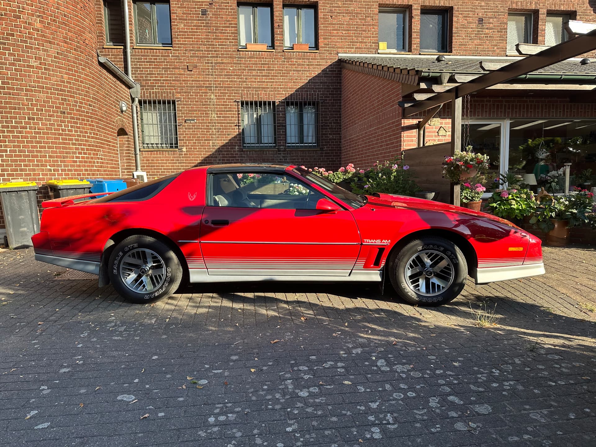 Roter 1984 Pontiac Firebird Trans Am in der Seitenansicht auf gepflastertem Hof